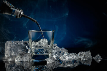 Crystal clear vodka or gin being poured over ice in a glass.