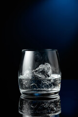 Vodka with ice on a black reflective background.