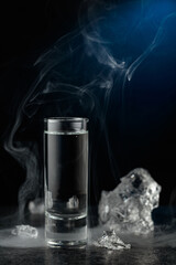Crystal clear vodka or gin in a glass on a black stone table.