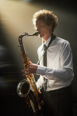 Vertical shot of adult male saxophonist dressed in white shirt and black tie passionately playing...