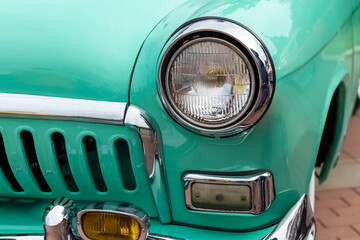 A vintage turquoise car features a round headlight and chrome accents while parked on a brick...