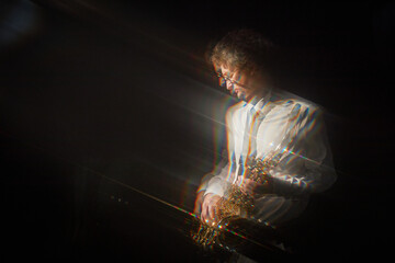 Motion blur shot of adult man in formal attire holding saxophone while standing in spotlight...