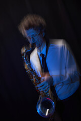 Vertical dynamic shot of expressive male jazz musician playing saxophone on stage illuminated by...