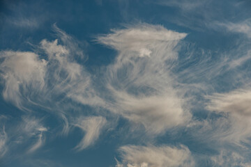 A mix of thin wispy cirrus clouds and soft puffy clouds float against a vibrant blue sky, creating...