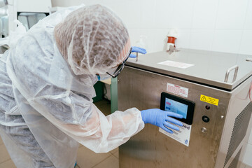 Technician in protective clothing setting pasteurization temperature and time on a breast milk...