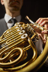 Obraz premium Vertical close up on fingers of male musician pushing valve levers of shiny French horn made of solid yellow brass, while performing deep mellow music on stage under bright spotlight