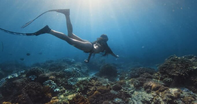 Female freediving undersea in blue ocean with sun rays in Raja Ampat
