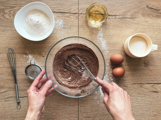 Hands of woman preparing chocolate dough at wooden table, top view.