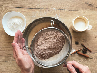 A woman's hands sift cocoa powder into homemade cookie dough.