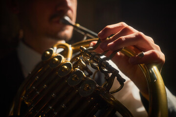 Close up on nimble fingers of male musician playing French horn pushing valve levers while performing music on stage in contrast lighting
