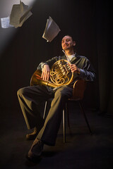 Vertical shot of professional male musician sitting in chair with French horn in studio while...