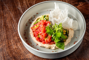 A beautifully arranged plate featuring creamy hummus topped with fresh tomato, cucumber, and herbs, garnished with crispy crackers, all set against a rustic wooden background.