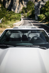 Fototapeta premium Front-view perspective through windshield on interior seats and steering wheel, natural daylight. View of Scenic cliffs and greenery in background.