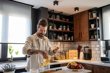 Young man peeling banana in modern kitchen, preparing healthy breakfast