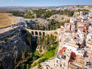 Scenic view of Gravina in Puglia, Italy, showcasing historic stone architecture, the iconic Roman bridge over the ravine, and the picturesque old town under a clear blue sky.