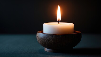 Candle illuminated on a wooden holder in dim light. Warm glow from the candle.