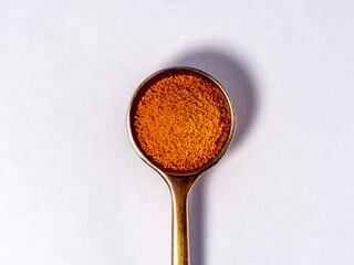 spoon filled with orange, finely ground powder, probably paprika, turmeric or chili spice. The spoon is on a light background. The photo is taken from above, with a central frame and good focus