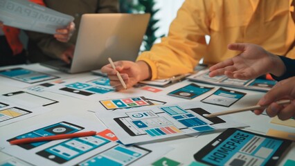 A diverse team collaborates on a digital project surrounded by wireframe mockups for web and mobile...