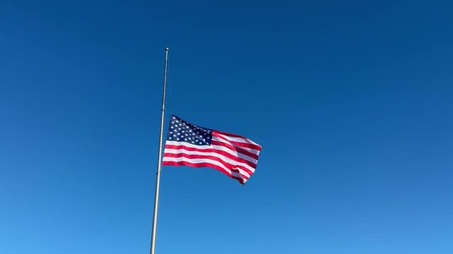 United States flag flying at half mast against clear blue sky. Minimal outdoor scene. Patriotic mourning and remembrance concept. Design for banner, postcard, invitation, card, poster with copy space