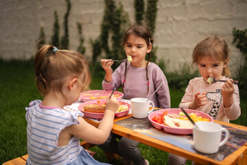 Three children enjoy a colorful meal outdoors on a sunny day