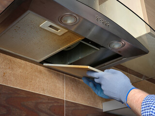 A worker in protective gloves opens a dirty kitchen hood grill.