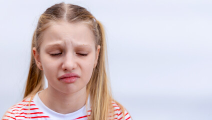 Young girl showing sadness with closed eyes. A girl with blonde hair and a striped shirt expresses...