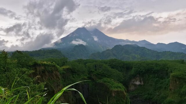 Time lapse of mount merapi in Yogyakarta, Indonesia with clouds and fog around it in the afternoon. Time lapse moment of a volcano covered in clouds with a foreground of hills and ravines