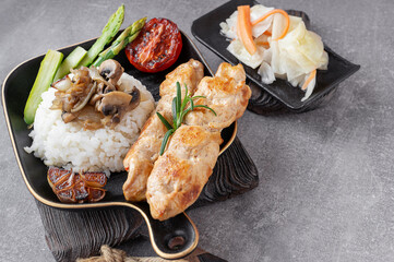 Grilled chicken kebabs with rice, fried mushrooms and vegetables, served on a black plate in a cosy setting