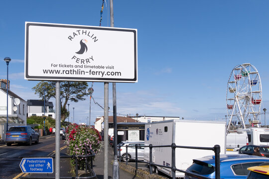 Ballycastle, UK - August 24th, 2024:  Rathlin Island Ferry sign at harbour, blue sky, sunny day, summer, with Ferris Wheel amusement park entertainment in place for the Ould Lammas Fair.