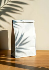 White paper bag placed on a wooden surface with a soft shadow of leaves creating a natural, artistic effect