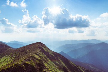 Breathtaking view of summer mountains with green slopes, bathed in warm morning light and misty blue ridges beyond. Spring mountains. Landscape photography