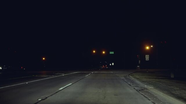 Nighttime footage from inside a moving car in a city. The vehicle slows and stops at a red light