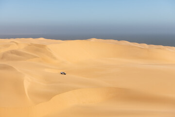 Lonely SUV car in Namibian dunes in Namib desert at Namib-Naukluft National Park of Namibia, Africa. Atlantic ocean on background. Landscape photography