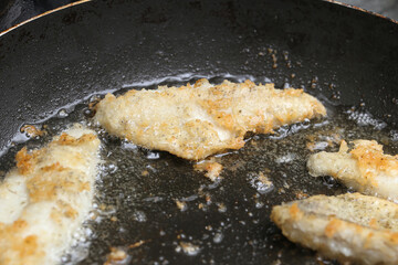 Fish fillets frying in oil. Crispy coating in hot pan. Homemade seafood preparation. Bubbling golden crust close up. Traditional cooking method. Fresh fried food during sizzling process.