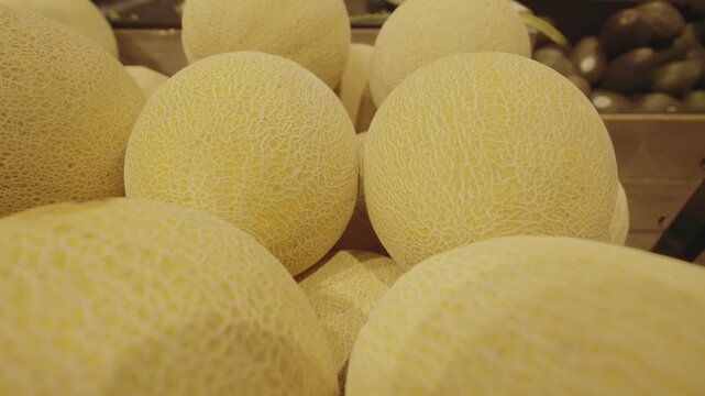 Fresh melons neatly arranged on a grocery store shelf, showcasing their smooth, ripe skin and juicy texture in a well-lit retail environment