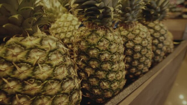 Fresh pineapples stacked on a grocery store shelf, showcasing their golden-yellow color, spiky green leaves, and textured skin in a well-lit retail environment