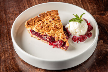 A delicious slice of berry pie topped with a scoop of vanilla ice cream and a sprig of mint, served on a simple white plate against a rustic wooden background.
