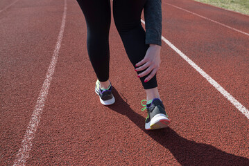 Fototapeta premium Photo of athletic female runner touching her leg experiencing pain due to ankle sprain, back view.