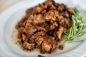 Wild boar pork meat morsels pieces in balsamic vinegar sauce, rosemary herb on white plate Sardinian traditional dish in Sardinia