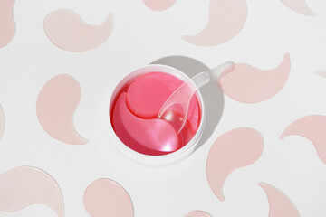 A white jar with pink hydrogel patches and a transparent spatula, set against a white background...