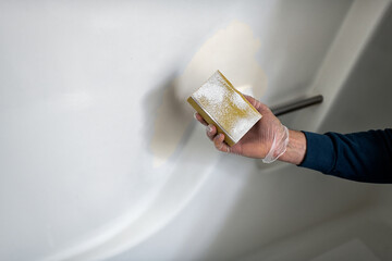 Man fixing bathroom tub wall white painted plastic doing remodeling renovation cleaning, resurfacing sanding the peeling paint