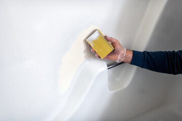 Man inside bathroom tub wall white painted plastic doing remodeling renovation cleaning, resurfacing sanding the peeling paint