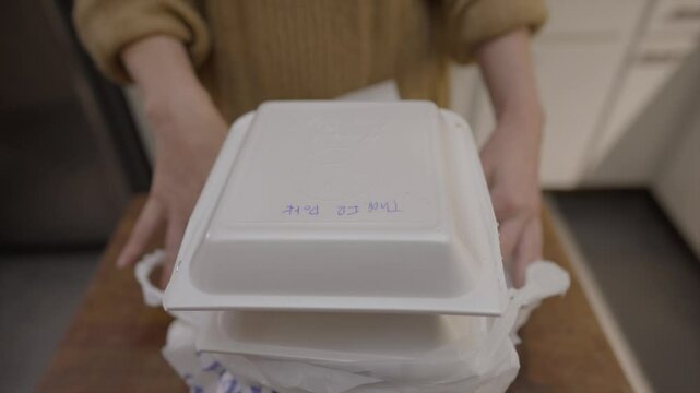This video shows a close up view of someone unwrapping a plastic bag full of carryout food and removing a styrofoam box.