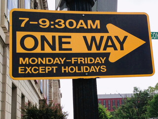 Fototapeta premium Yellow and black one way street sign regulating traffic flow on weekdays from 7 to 9:30 am