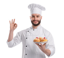 Happy confectioner in uniform holding delicious profiteroles with strawberries and showing ok gesture on white background