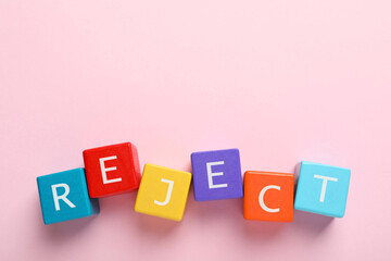 Word Reject made of colorful cubes with letters on pink background, top view. Space for text