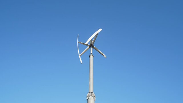 A modern vertical axis wind turbine rotates under a clear sky, showcasing renewable energy benefits