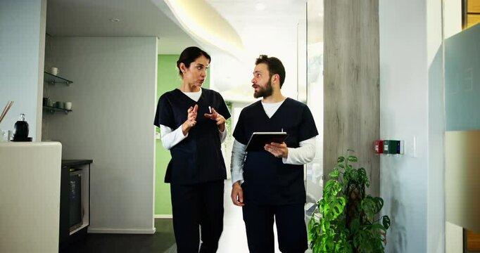Nurses, man and woman in discussion with tablet, walking and checking online schedule in dental office. Advice, dentist and hygienist in lobby with digital app, conversation and healthcare planning