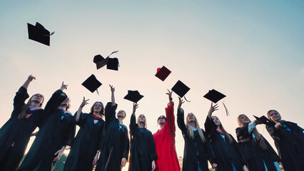 Photo of joyful graduates throwing their caps in the air under a bright blue sky, commemorating...