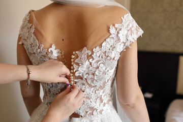 A bridesmaid at a wedding helps the bride lace up her dress corset